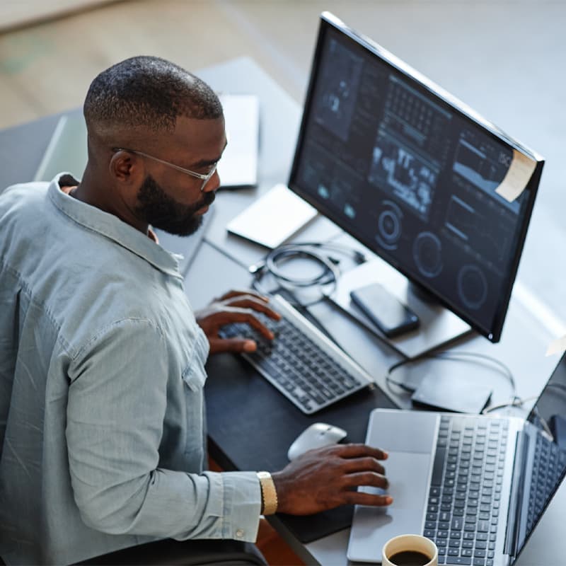 Minimal high angle view at African American software developer working with computers and data systems in office