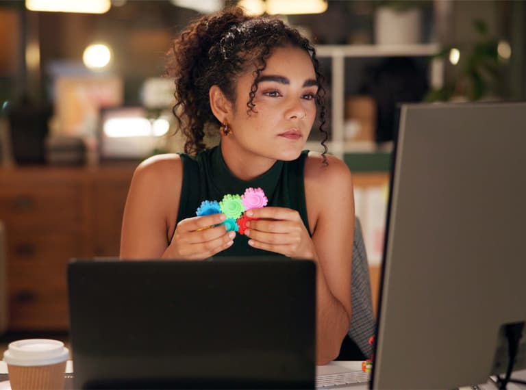 Business woman, laptop and thinking with pop toy, creative agency and ideas for night brainstorming. Girl, brand consultant and multi screen computer with project, proposal and office fidget spinner.