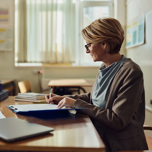 Mature female teacher grading exam papers at high school.