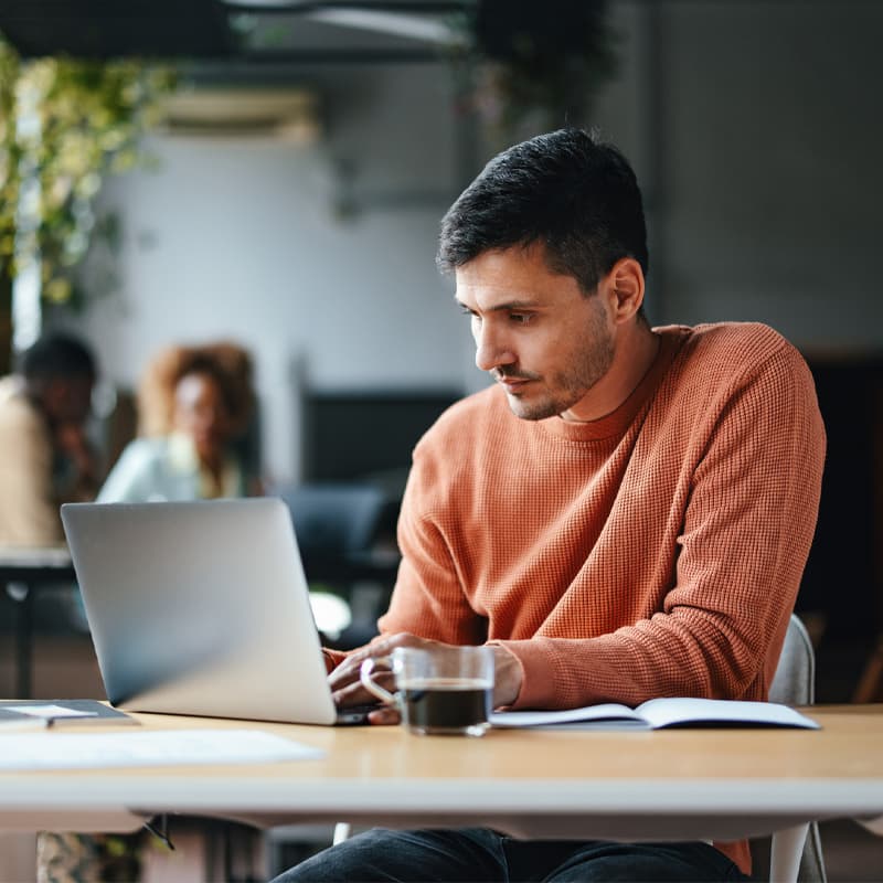 A serious Caucasian entrepreneur typing on his laptop while sitting at the office desk.