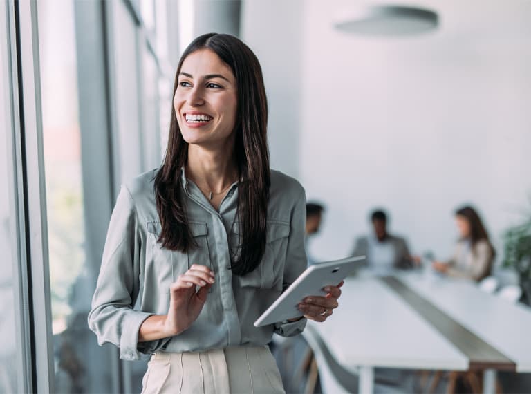 Shot of a smiling businesswoman standing in front of her team and using digital tablet. Portrait of successful businesswoman standing with her colleagues working in background.