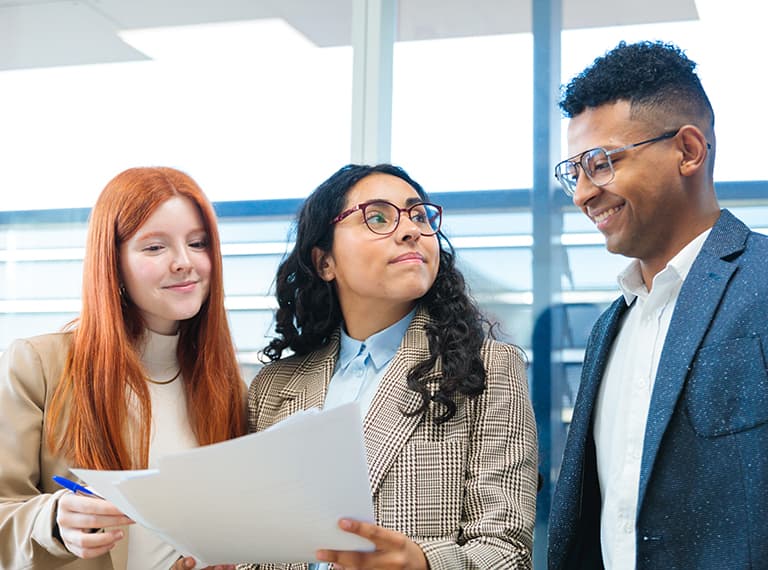 Three diverse professionals in business attire reviewing a document together in a bright modern office setting.