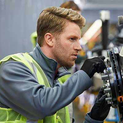Technician in gray jacket and high-visibility vest examining equipment in an industrial setting.