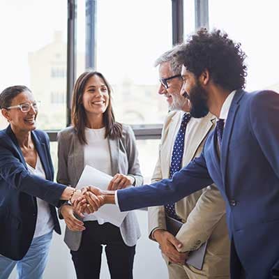 Diverse business professionals shaking hands in a bright office, smiling and celebrating a successful partnership or deal.